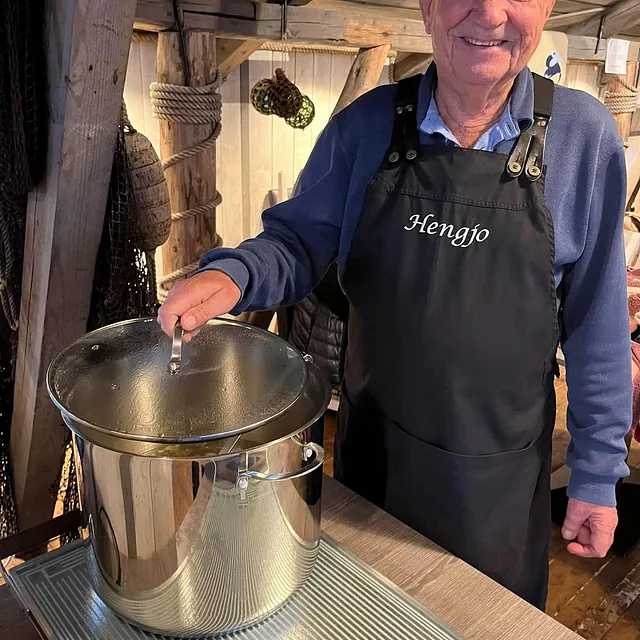 Mann i forkle smiler ved stor gryte på kjøkkenbenk