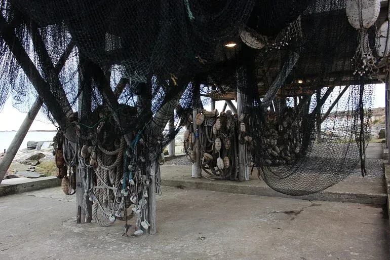 Fiskeredskaper og nøter henger til tørk under et naust